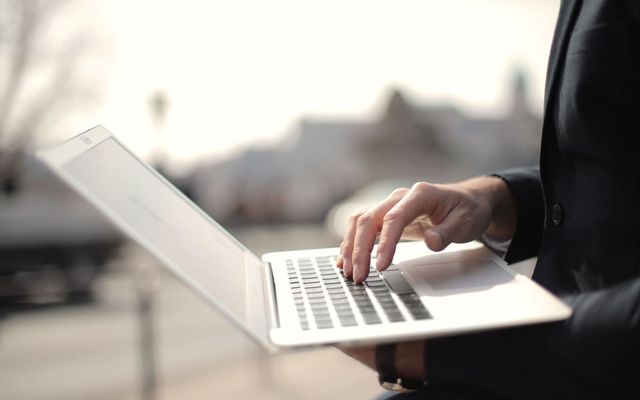 A business professional typing on a laptop in an outdoor setting, symbolizing remote work.